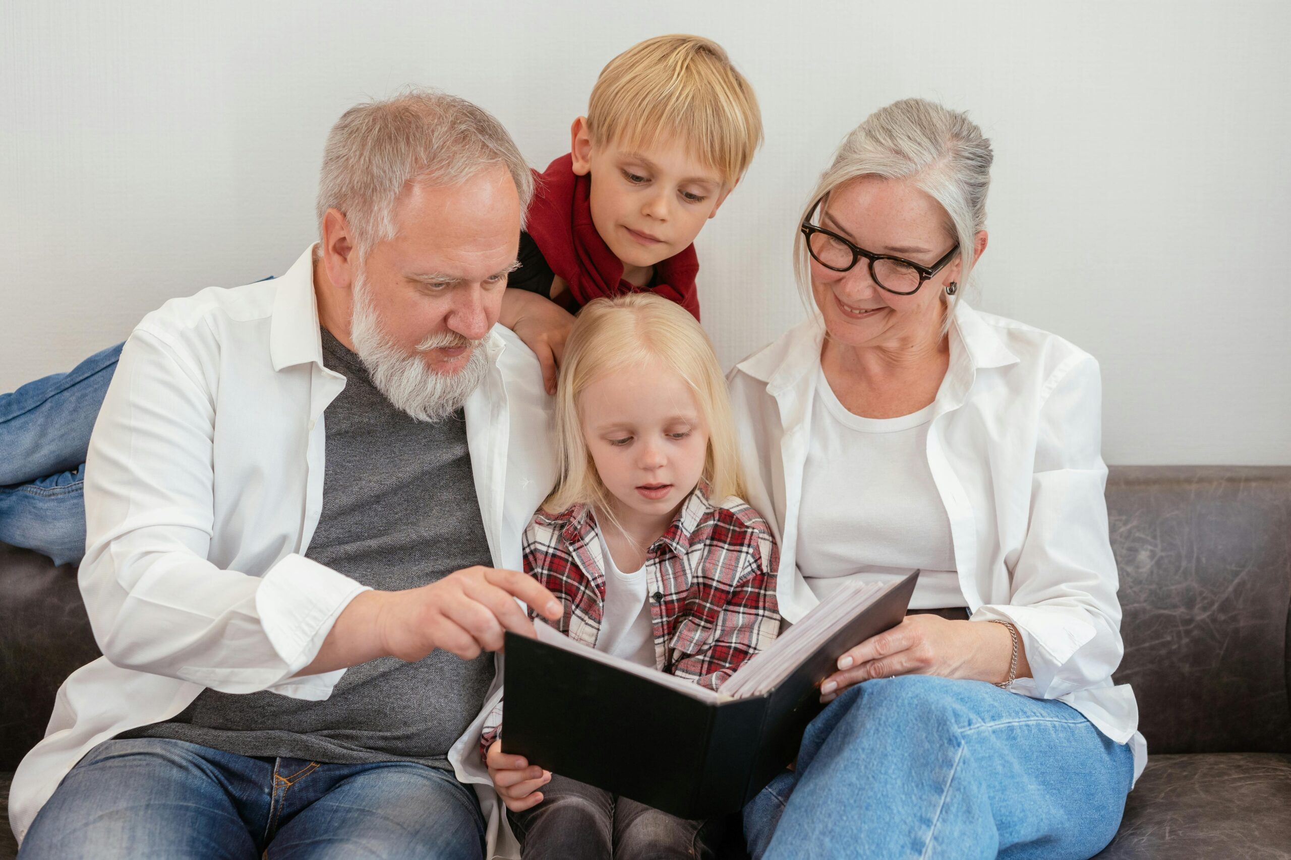 pexels-photo-8307717-8307717 Grandparents and grandchildren reading a photo album on the couch, embracing family bonds and love.
